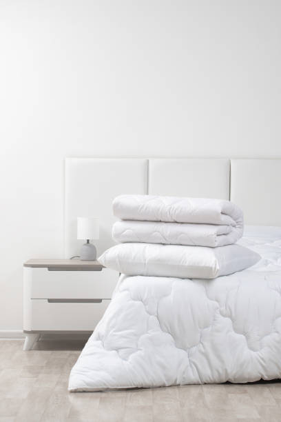 istock A bed with white pillows and a blanket, next to a bedside table with a lamp, daylight 2195252311