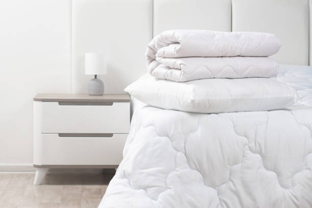 istock A bed with white pillows and a blanket, next to a bedside table with a lamp, daylight 2195252318