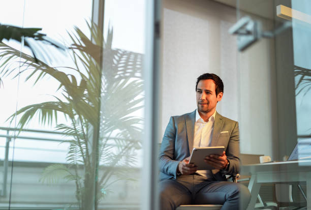 istock Businessman in Moody Lighting Using Digital Tablet in Office 2195255291