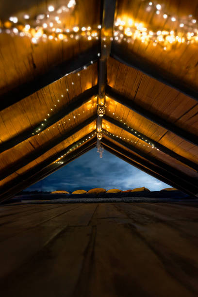 A beautifully lit open attic with glowing string lights, wooden beams, and soft cushions, offering a cozy ambiance and a serene view of the night sky.