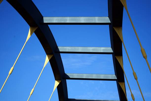 istock Detail of a modern arch bridge construction with yellow elements against a bright blue sky. An elegant combination of engineering and architecture. 2195260362