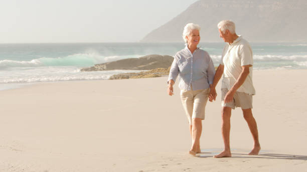 istock Romantic Senior Couple On Summer Vacation Holding Hands Walking Along Beach 2195260577
