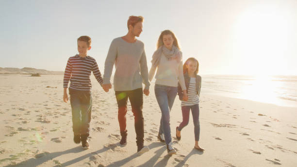 istock Family Walking On Winter Beach Holding Hands With Flaring Sun 2195260797