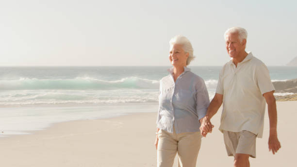 istock Romantic Senior Couple On Summer Vacation Holding Hands Walking Along Beach 2195261991