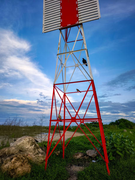 istock A striking red and white metal tower stands tall against a serene blue sky, with birds perched on its framework. 2195262908