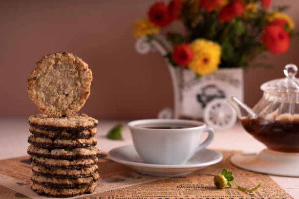photo Enjoy an Elegant Tea Time Experience with Chocolate Cookies and Herbal Tea alongside a Colorful Floral Arrangement for Delightful Moments