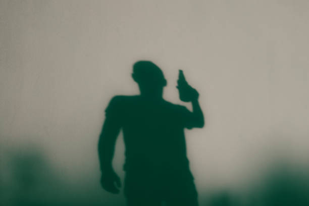 istock Shadow figure. A man drinks alcohol from a bottle. Back view of shadow. Young man with beer bottle 2195266705