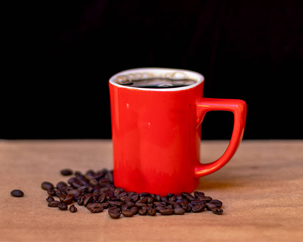 istock A vibrant red coffee mug filled with freshly brewed black coffee, surrounded by scattered roasted coffee beans on a wooden surface. 2195268782