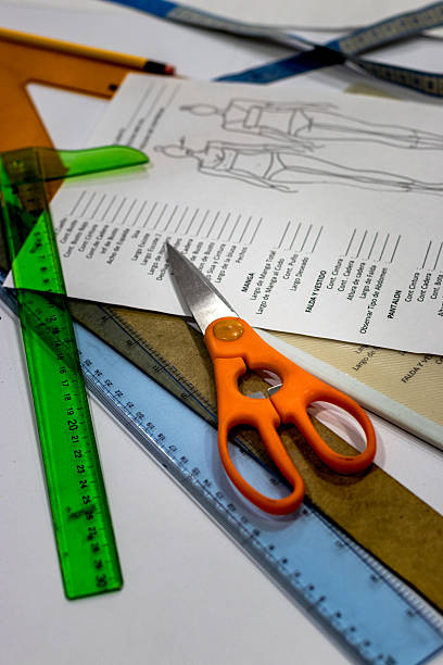 A workspace featuring essential tailoring tools, including vibrant orange scissors, rulers, and a pattern sheet with garment measurements. Ideal for themes of sewing