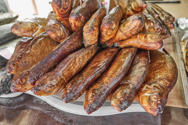 Half of a cold smoked freshwater fish cut lengthwise without a spine on a skin on a white dish on a gray background, top view