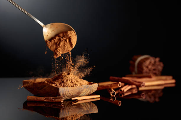 Cinnamon powder is poured into a wooden dish. Black background with copy space.