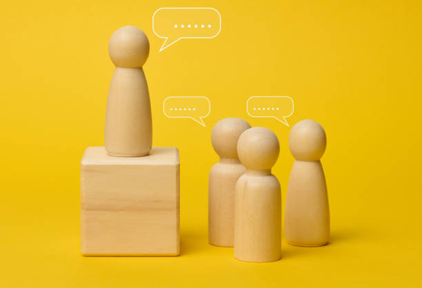 istock Wooden figures on a yellow background symbolize communication and leadership, one figure stands on a pedestal 2195279213