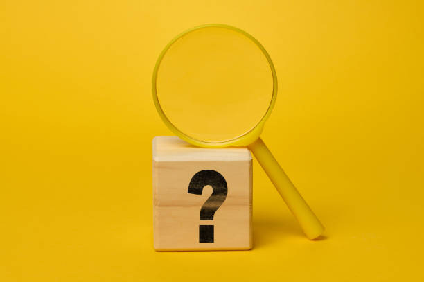 istock Plastic magnifying glass on yellow background and wooden cube with question mark 2195279522