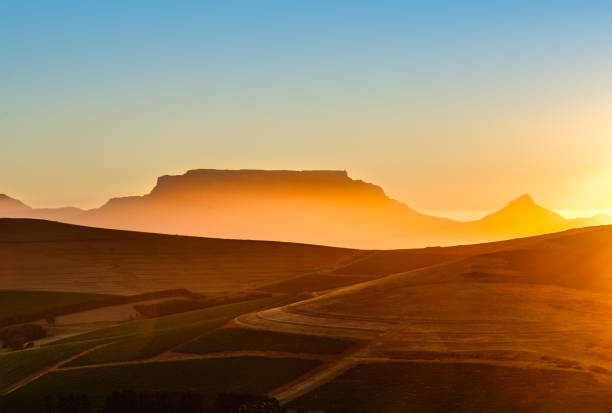 Authentic colors of dusk in the sky over the famous landmark of Table Mountain, Cape Town, as seen from the beach at Bloubergstrand to the north of the city. The waves coming in from the sea have been softened by a long exposure.