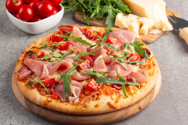istock Pizza with prosciutto, ham, arugula, spinach, tomatoes, pesto, cheese and parmesan. Italian cuisine 2195286918