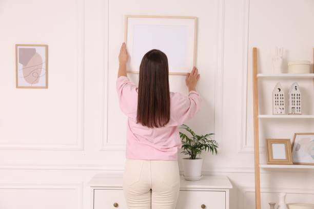 istock Woman hanging picture frame on white wall at home, back view 2195288410