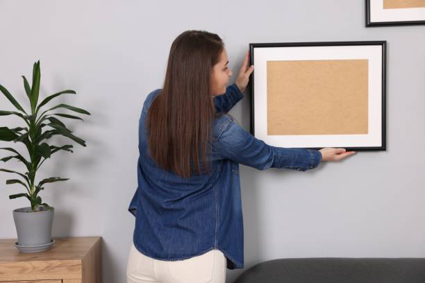 istock Woman hanging picture frame on gray wall at home 2195288466