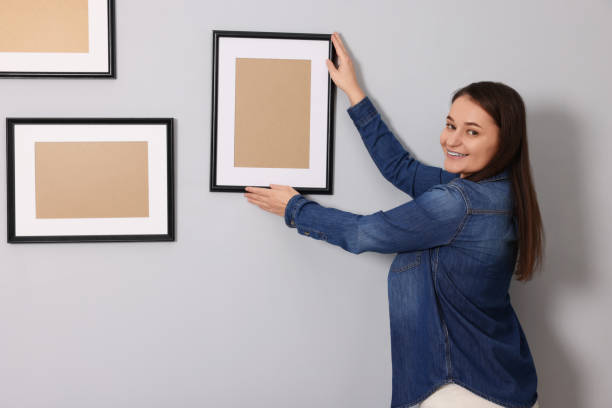 istock Woman hanging picture frame on gray wall 2195288497