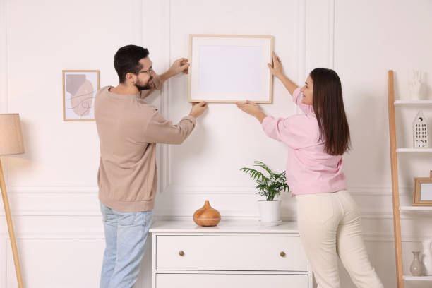 istock Man and woman hanging picture frame on white wall at home 2195288519