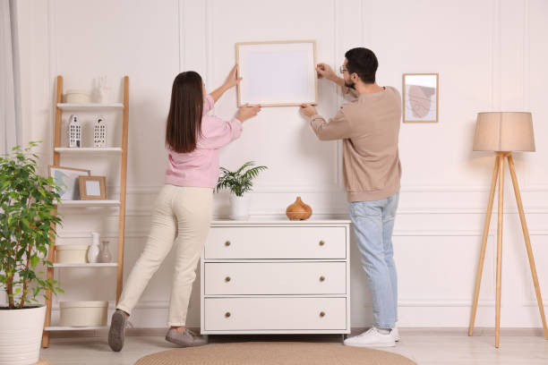 istock Man and woman hanging picture frame on white wall at home 2195288575