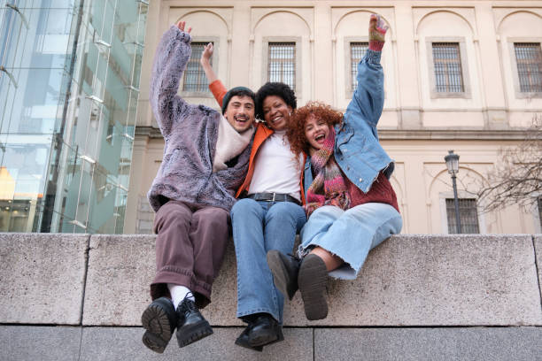 istock Happy multiethnic friends raising arms and screaming while sitting on a wall 2195291913