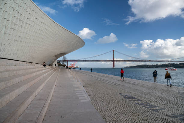 06.01.2025 Lisbon, Portugal. The Museum of Art, Architecture, and Technology's sweeping curves harmonize with the majestic 25 de Abril Bridge, showcasing Lisbon's architectural ingenuity and breathtaking riverside scenery.