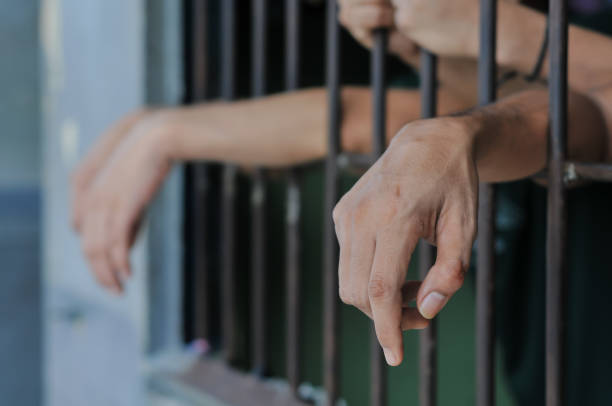 istock hands of a prisoner behind prison bars on black background 2195304693