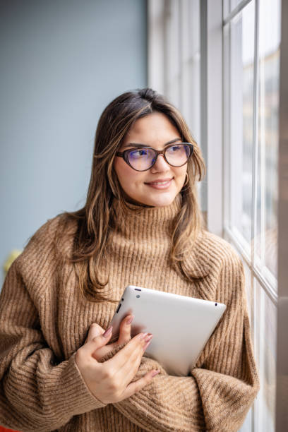 istock Woman in cozy sweater holding tablet while enjoying natural light by the window 2195305904