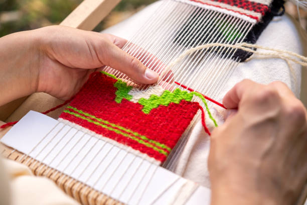 Close-up of a woman weaver's hand using a weaving needle on a hand loom. Selective focus.