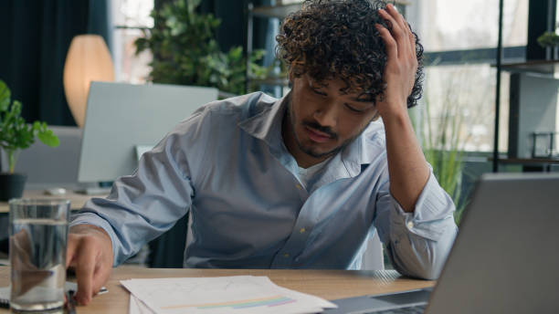 istock Frustrated Indian business man Arabian businessman at office desk difficult work solve issue problem with paperwork documents loss finances budget trouble feel stress disappointed negative emotions 2195306350