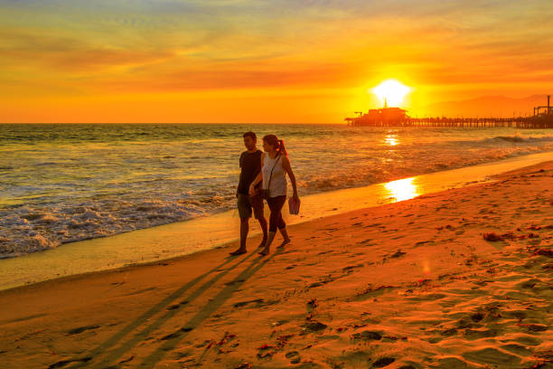 Santa Monica, California, USA - August 8, 2018: romantic couple walking on seashore of Santa Monica Pier, Pacific Coast. California honeymoon tourism. Sunlight over the sea on the horizon.
