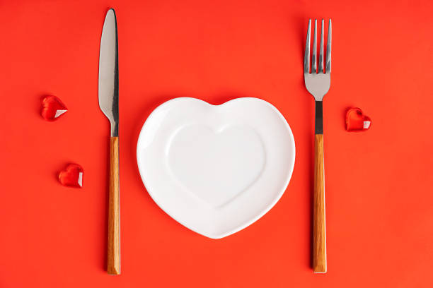 istock Overhead view of white empty heart shaped plate served with fork and knife on bright red background 2195311646