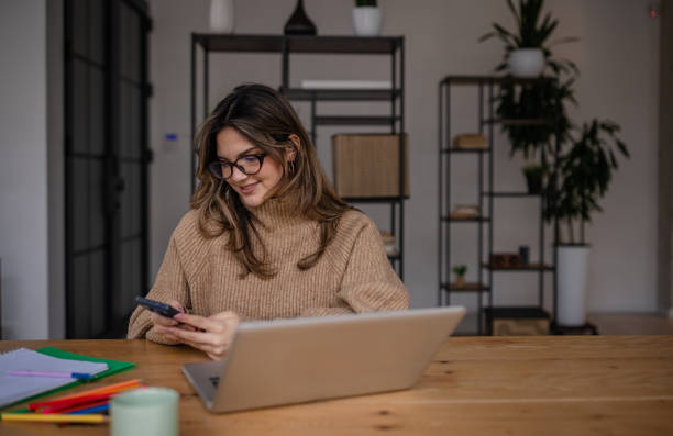 istock Young woman focused on her smartphone while working from a cozy, modern home office in the afternoon light 2195313168