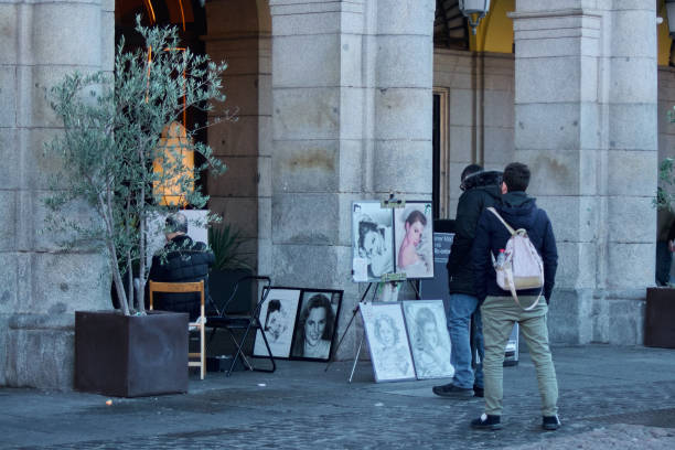 Madrid. Spain - January 22, 2025: Street artist painting in Madrid Plaza Mayor, with observers engaging in the creative process The lively atmosphere highlights the rich cultural heritage of the city.