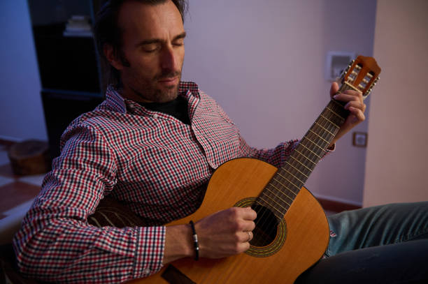 istock Man playing acoustic guitar while sitting in a cozy room 2195329118
