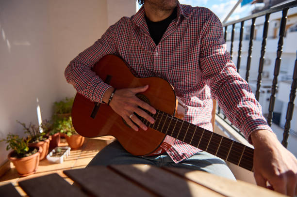 istock Man sitting with a classical guitar on a sunny balcony patio 2195329146