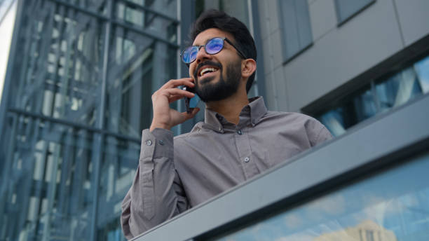istock Joyful Indian man talking mobile phone on office terrace outdoors happy smiling Arabian businessman employer ceo executive talk smartphone in city friendly business conversation cellphone call outside 2195330449