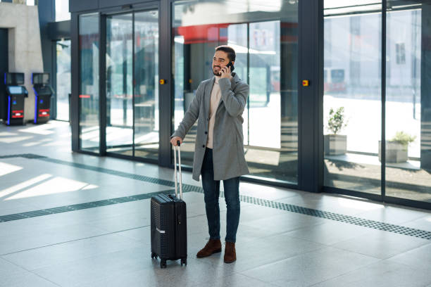 istock Businessman talking on phone while pulling suitcase at airport 2195330905