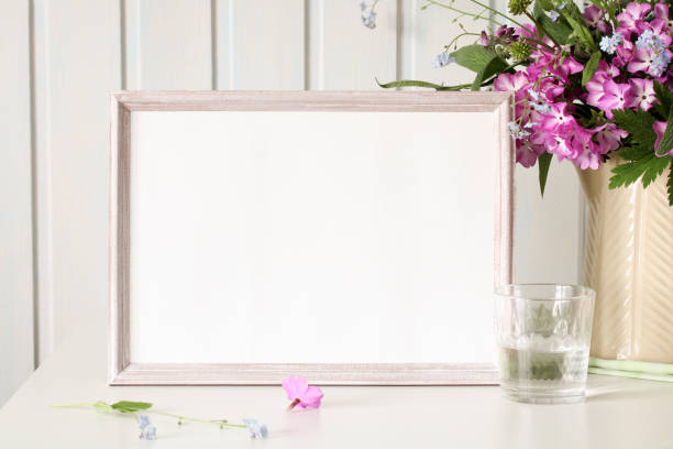 istock Horizontal white frame mockup with flowers and glass of water on white table 2195332222