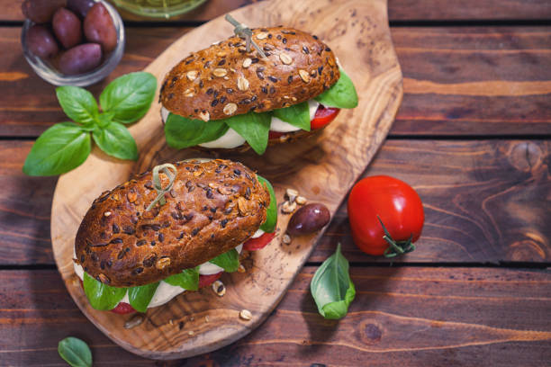 bruschetta topped with fresh tomato, avocado and basil leaves, with scattered peppercorns on a rustic wooden surface.