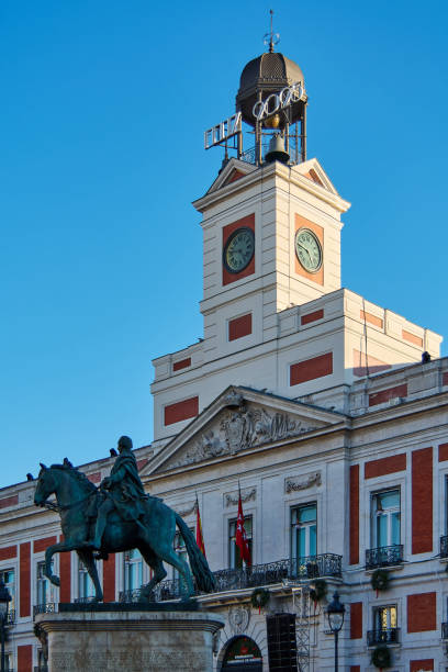 Madrid. Spain - January 22, 2025: Puerta del Sol, Madrid, featuring a prominent clock tower and equestrian statue of King Charles III. The building is adorned with flags