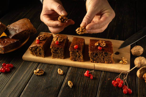 istock In a cozy kitchen setting, hands arrange glossy walnuts and vibrant red berries atop freshly baked squares of cake, evoking a sense of warmth and creativity in dessert making 2195334720