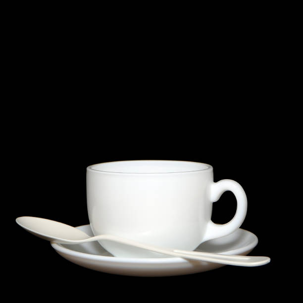 Cup and saucer with spoon isolated on black background closeup view