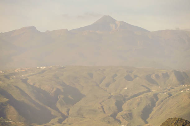 The mountain range is covered in green vegetation and has a misty, hazy appearance. The sky is cloudy and the sun is low in the sky