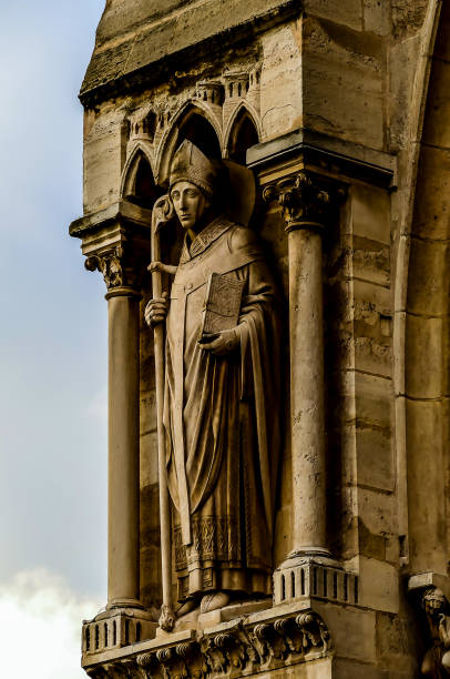 A statue of a man holding a book. The statue is on a building. The statue is of a religious figure