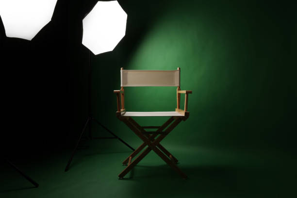 istock Photo studio with green screen background and wooden stool against professional lighting equipment. Interior of photo studio with professional lighting equipment and director chair with green backdrop 2195338681