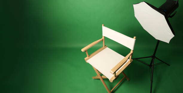 istock Photo studio with green screen background and wooden stool against professional lighting equipment. Interior of photo studio with professional lighting equipment and director chair with green backdrop 2195338683