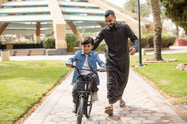 istock Saudi arabian father in thawb supporting his son while cycling at the park 2195339592