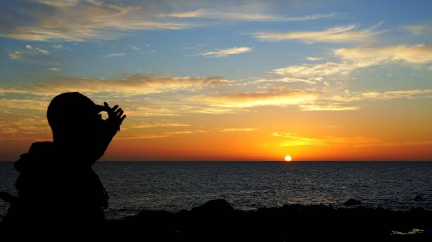 Silhouette of a mature man shielding his eyes from the setting sun over the ocean in the Canary Islands, creating a dramatic and inspiring scene of travel and exploration