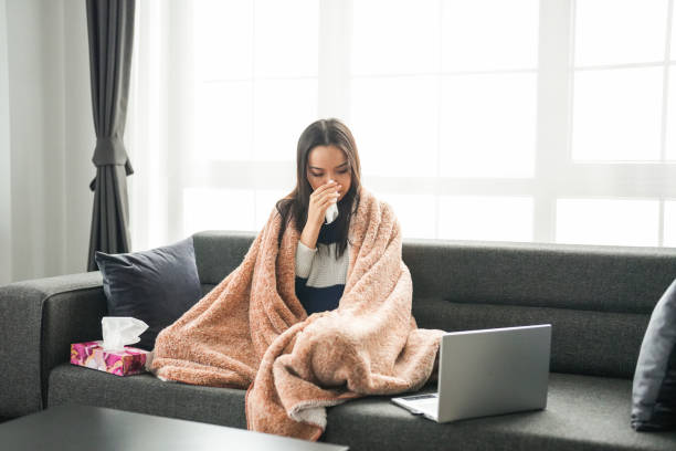 istock Young woman with flu sitting on couch looking at laptop 2195339940